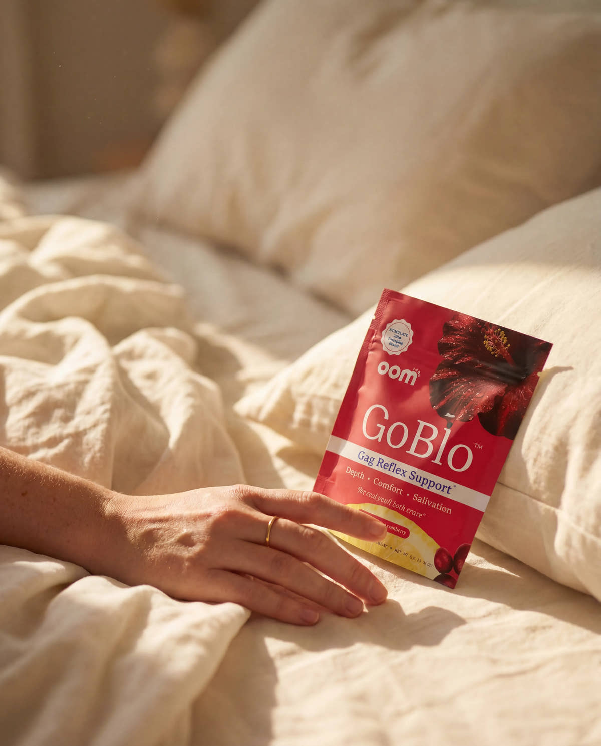 Hand reaching for a GoBlo stick pack on a bed